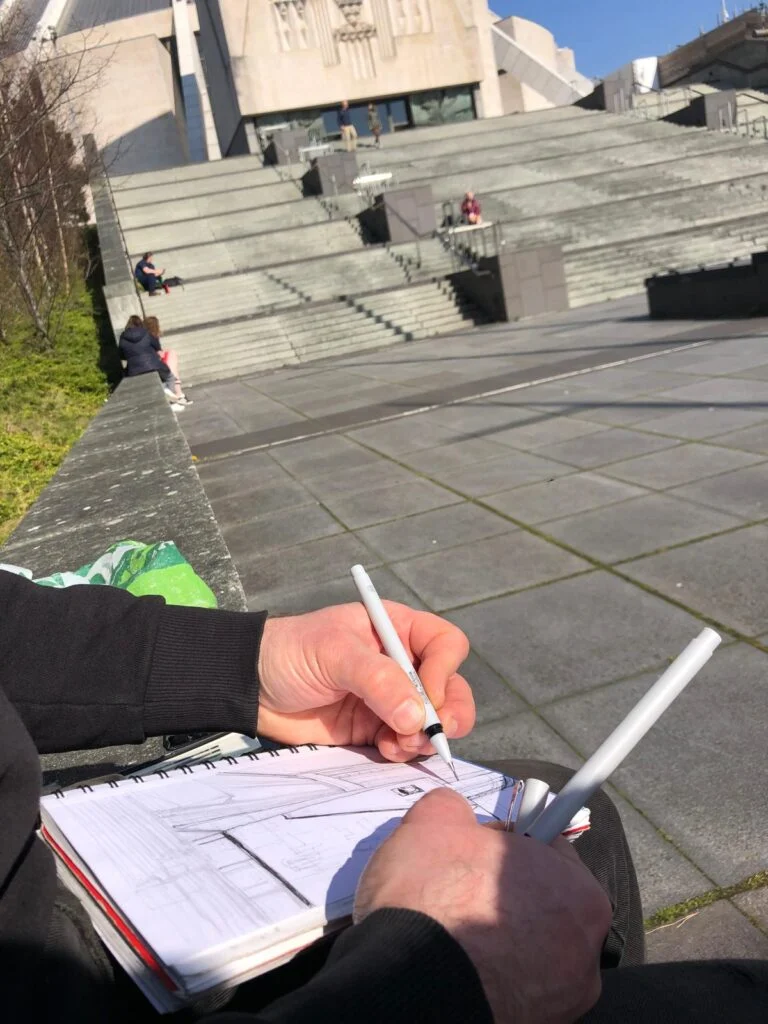 Hands drawing in a sketchbook outside Liverpool Metropolitan Cathedral